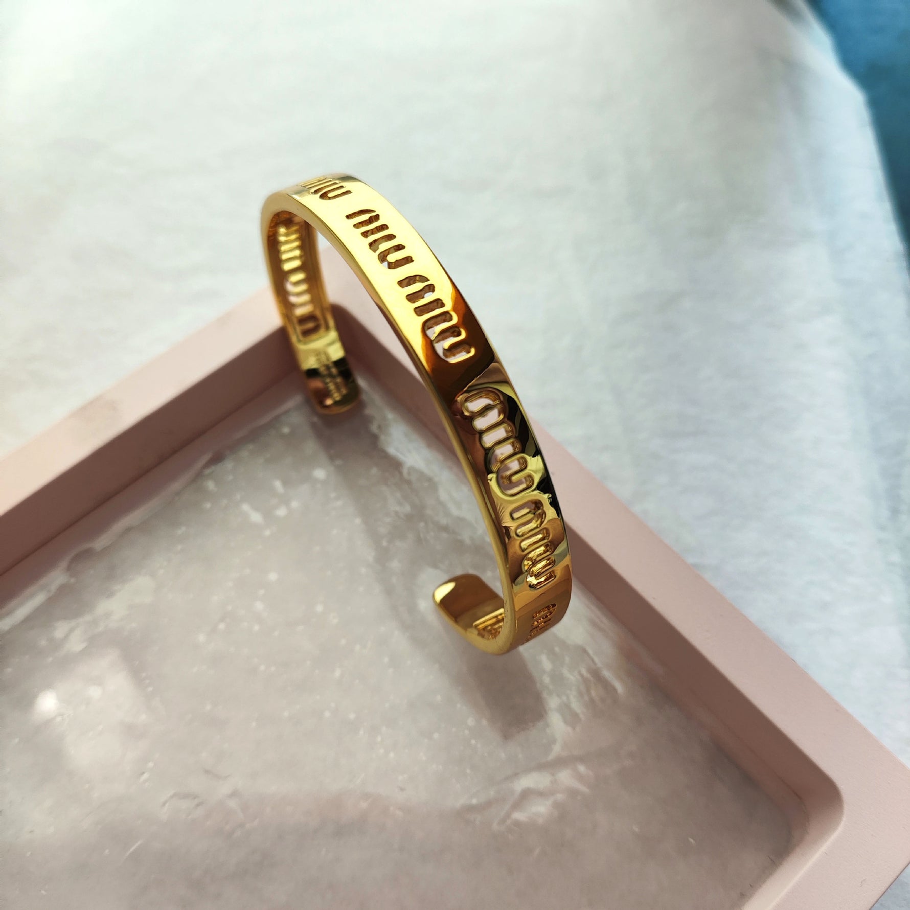 Gold openwork logo bangle, side view showing engraved “miu” lettering strip