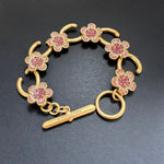 Rosa Blumenarmband mit goldfarbenen Gliedern und funkelnden Steinen, mit Stabverschluss