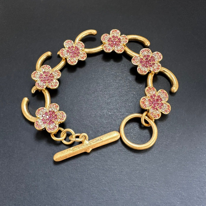 Rosa Blumenarmband mit goldfarbenen Gliedern und funkelnden Steinen, mit Stabverschluss