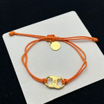Orange woven adjustable drawstring bracelet with gold clover charm and small round tag
