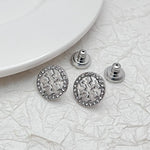Round logo stud earrings in white-gold tone, rhinestone border and openwork emblem