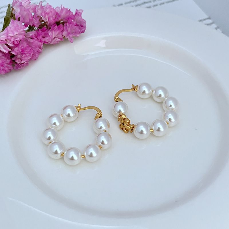 Gold hoop earrings with white round pearls and dangling logo-style charm