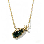 Gold-tone necklace close-up with green gem-like rectangular pendant and side horn accents