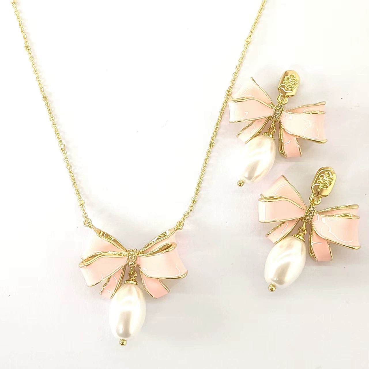 Bow pendant necklace with pink enamel and white pearl drop, plus matching earrings