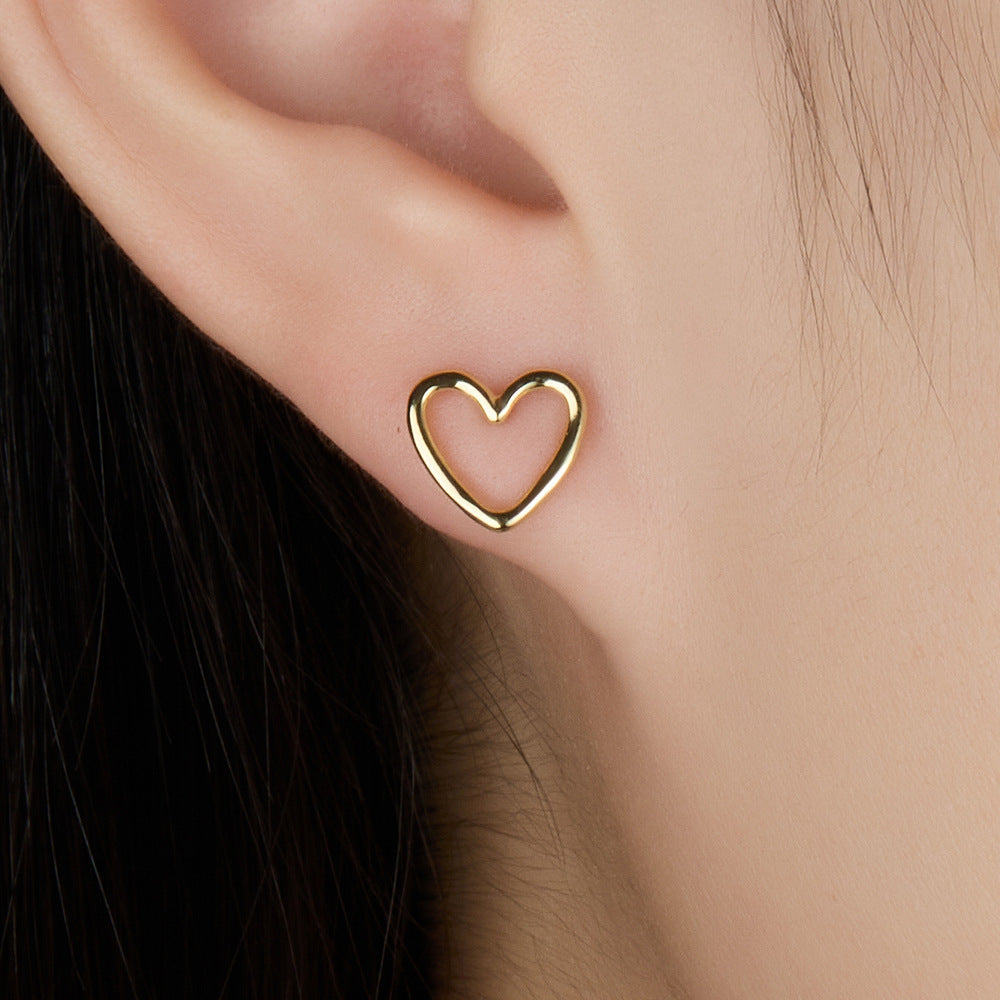 Heart-shaped stud earrings, gold tone, hollow heart motif worn on ear