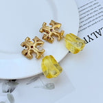 Yellow irregular acrylic logo pendant earrings with gold-tone geometric cross and curved drop
