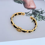 Offenes Cuff-Armband aus gewobenem Leder, goldfarbene Glieder mit schwarzen Akzenten
