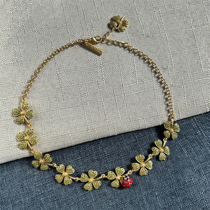 Goldtone necklace with green textured four-leaf clovers and a red ladybug charm