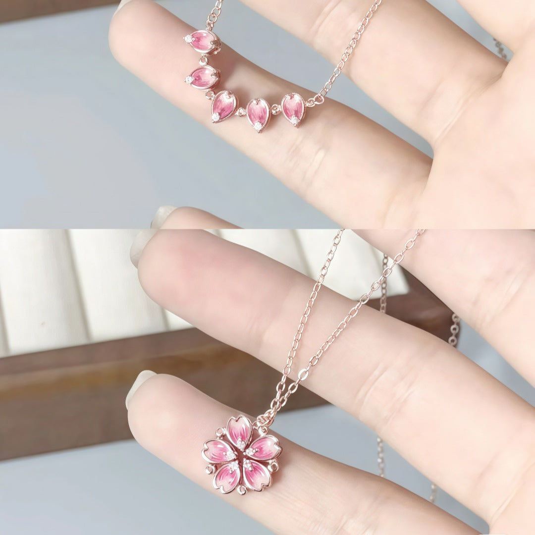 Flower pendant necklace with pink enamel petals on rose-gold chain, worn on hand