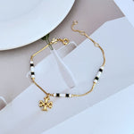Gold-tone bracelet with white enamel bead stations and flower-like logo charm