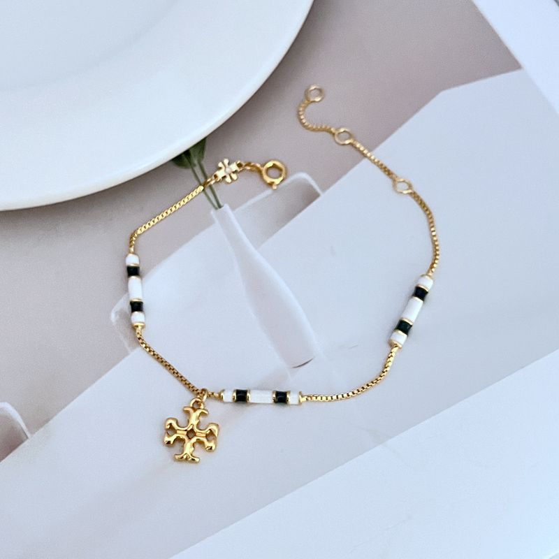 Gold-tone bracelet with white enamel bead stations and flower-like logo charm