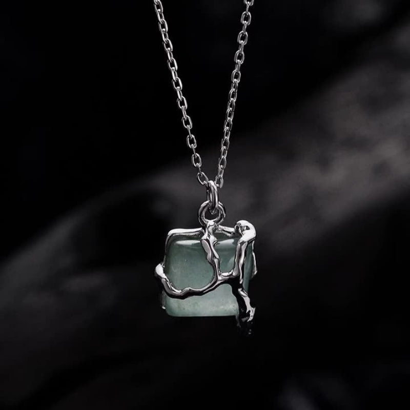 Necklace with a pendant featuring a green stone and silver branch-like design on a dark background