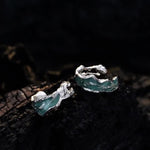 Silver earrings with greenish-blue accents on a dark textured surface