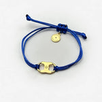 Woven enamel bracelet with blue braided cord, gold logo charm, and round engraved tag.