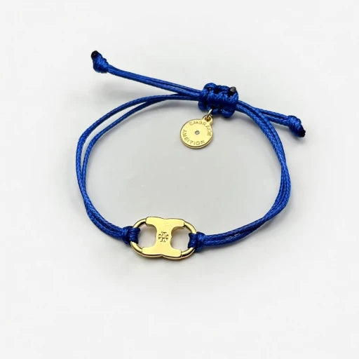 Woven enamel bracelet with blue braided cord, gold logo charm, and round engraved tag.