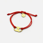 Woven enamel bracelet with red braided cord, gold logo charm, and round engraved tag.