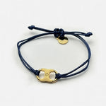 Woven enamel bracelet with dark blue braided cord, gold logo charm, and small round tag.