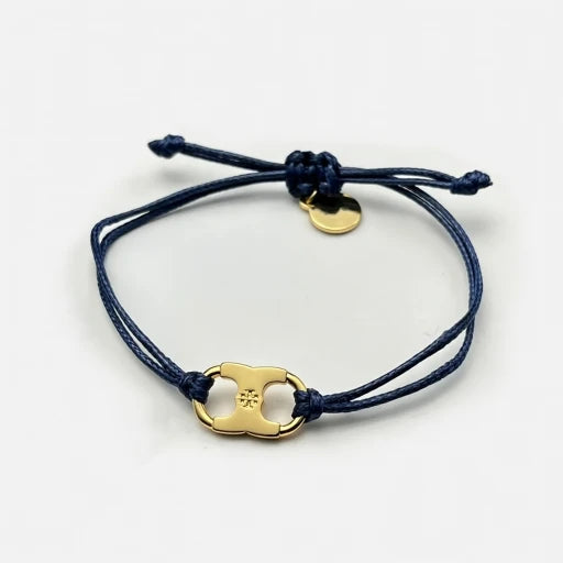 Woven enamel bracelet with dark blue braided cord, gold logo charm, and small round tag.