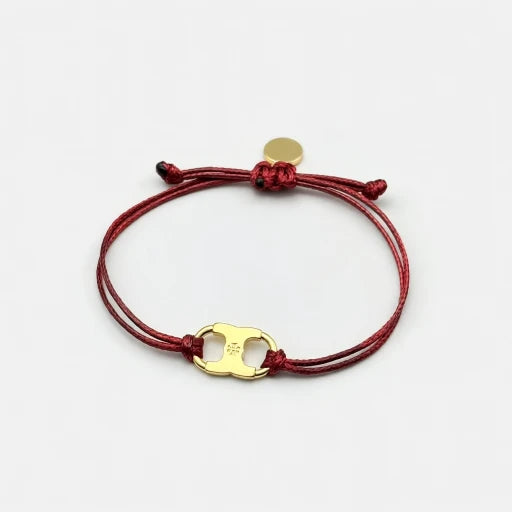 Woven enamel bracelet with red braided cord and gold logo charm with small enamel detail.