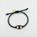 Adjustable drawstring bracelet with gold enamel toggle charm on black cords