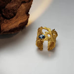 Gold-tone hollow lava ring with blue gemstone centerpiece, openwork design