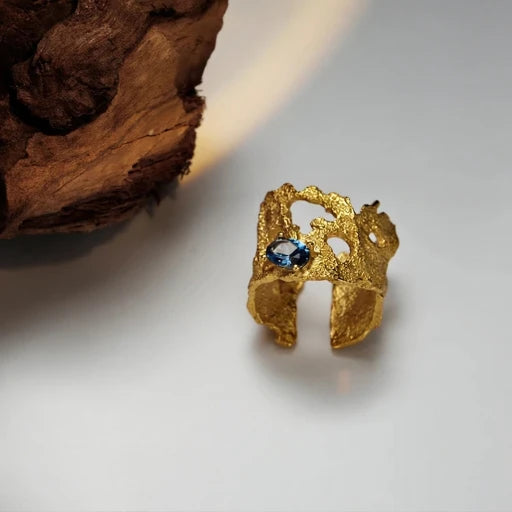 Gold-tone hollow lava ring with blue gemstone centerpiece, openwork design