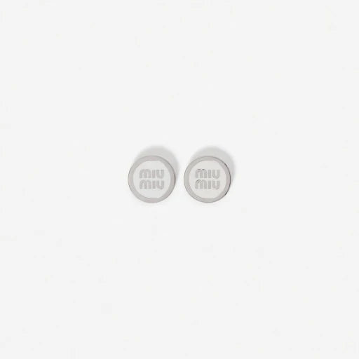 Silver-tone round enamel stud earrings with light gray 'miu miu' logo center.