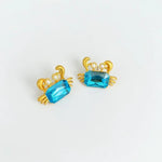 Crab-shaped crystal stud earrings with gold-tone settings, pearls, and a bright blue gem