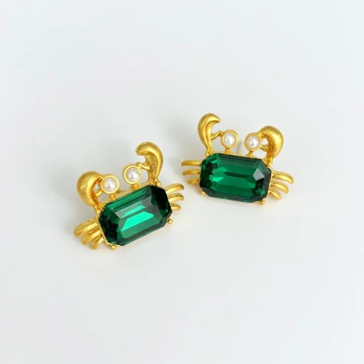 Crab-shaped crystal stud earrings with gold-tone settings, pearls, and a deep green gem
