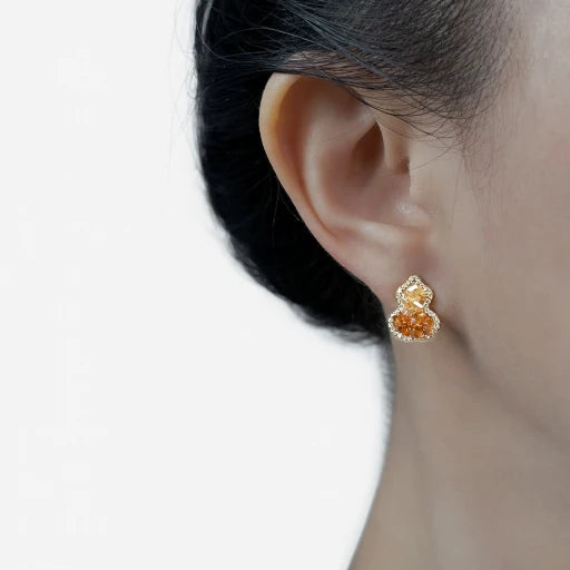 Gourd-shaped crystal stud earrings on ear, amber orange sparkle with rhinestone detail