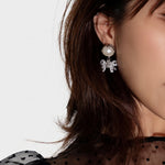 Crystal bow dangle earrings with white pearl on silver-tone studs, close-up.