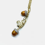 Gold pendant necklace close-up with squirrel charm, glitter caps, and pinecone beads