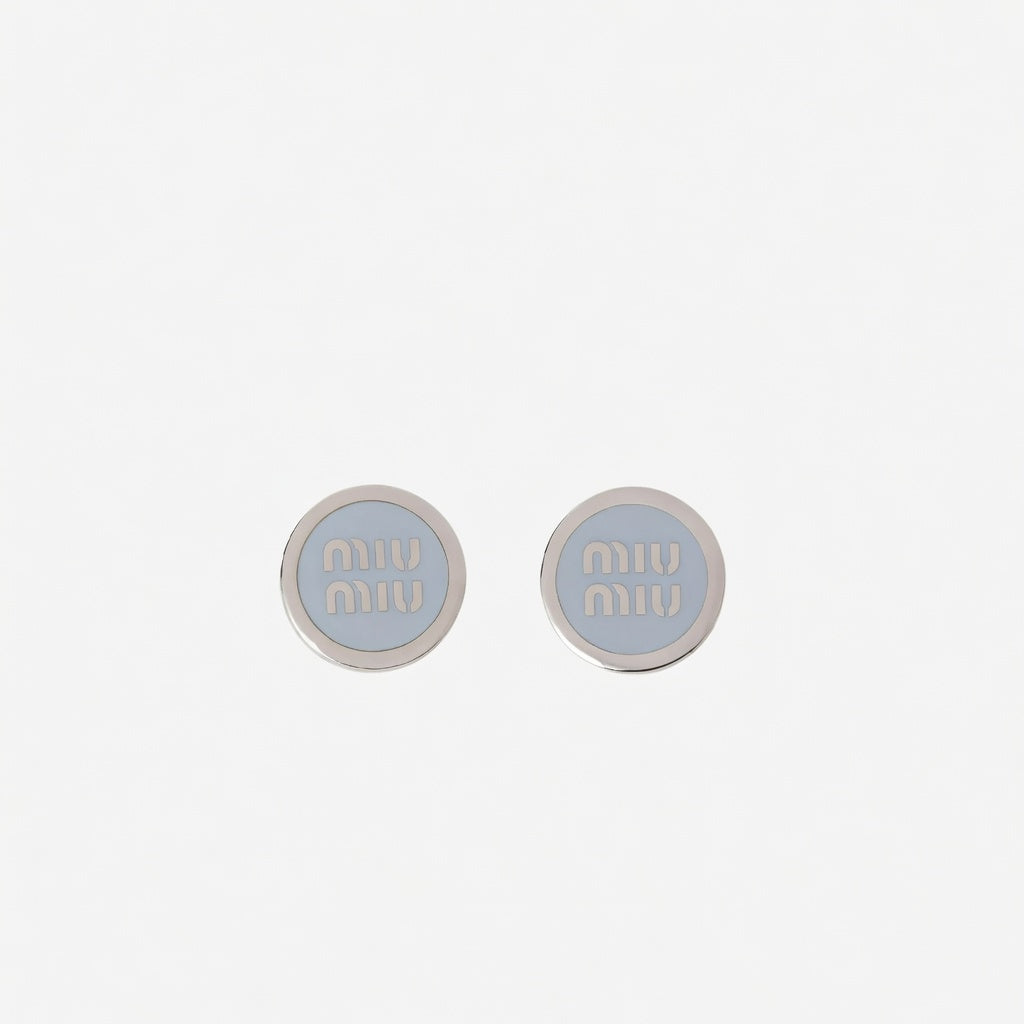 Silver-tone round enamel stud earrings with light gray 'miu miu' logo center.