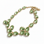 Gold teardrop crystal necklace with green stones and linked floral clusters.