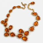 Gold teardrop crystal necklace with orange stones and linked floral cluster rows.