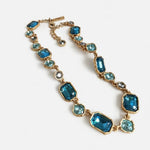 Gold-tone square crystal necklace with teal-blue faceted stones and small round accents.