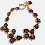 Gold teardrop crystal necklace with dark purple stones and linked floral clusters.