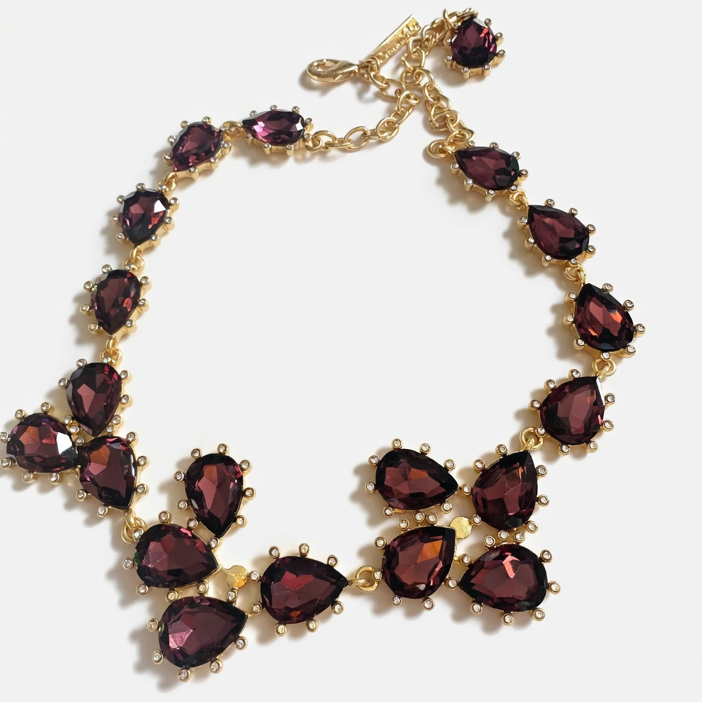 Gold teardrop crystal necklace with dark purple stones and linked floral clusters.