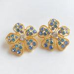 Floral stud earrings with blue pavé petals and round clear center, gold-tone setting.